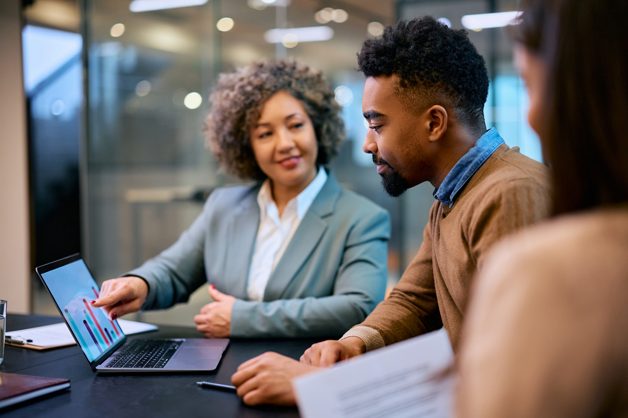 Smiling black man and financial consultant analyzing his investments on laptop in the office.